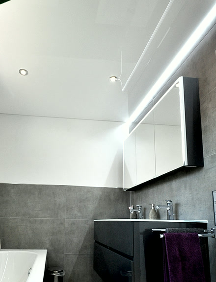 Bad mit spiegelnder Hochglanz-Spanndecke, Einbauspot und einem LED-Streifen über dem Spiegelschrank