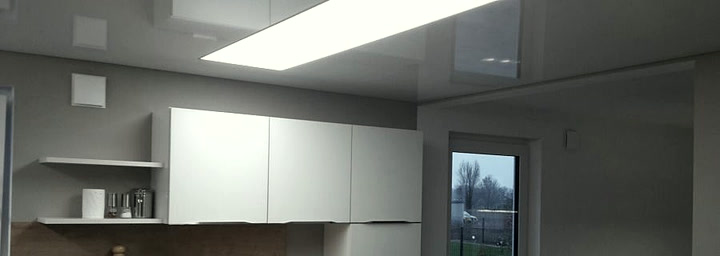 Küche mit Holzarbeitsplatte und einem großen, leuchtenden Deckenfeld in der weißen Spanndecke