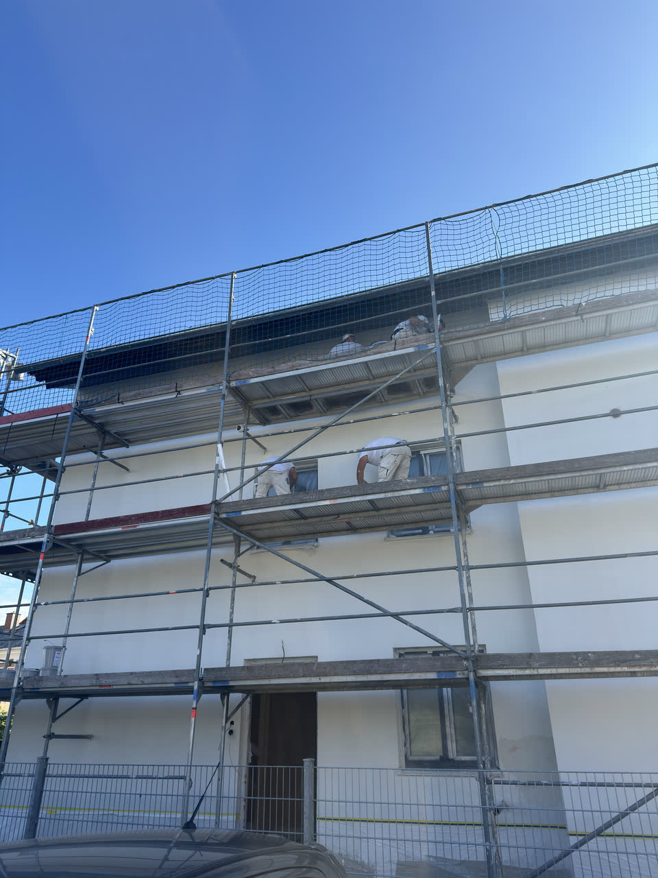 Eingerüstete Hausfassade mit frisch aufgezogenem weißem Putz, darüber blauer Himmel