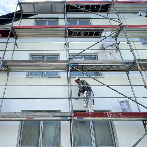 Handwerker arbeiten auf zwei Gerüstlagen an der weißen Fassade