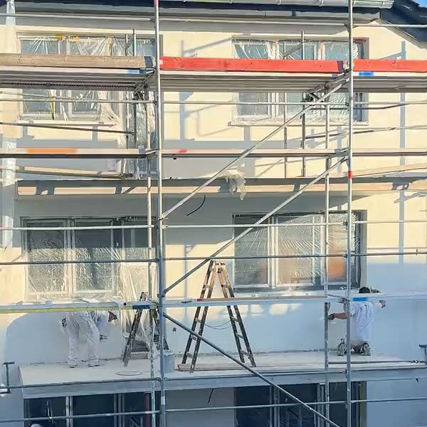 Eingerüstetes Mehrfamilienhaus in Bürstadt im Abendlicht, Handwerker auf dem Gerüst
